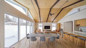 A modern kitchen with wooden cabinets, a large island with bar stools, and a dining area with a round table and chairs. - Sakuraya (Hakuba)