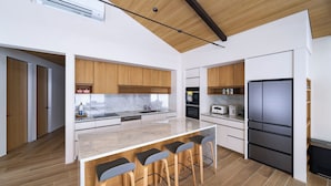A modern kitchen with wooden cabinets, a marble countertop, and a built-in island with bar stools. - Sakuraya (Hakuba)