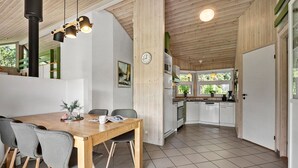 Moderni keittiö, jossa on valkoiset kaapit, ruokailutila puupöydällä ja harmailla tuoleilla sekä seinällä oleva kello.