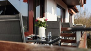 A table with a vase of flowers, two glasses, and a magazine on a balcony. - Quartier 7 apartment in a quiet location and access to the sea time (Büsum)