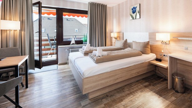 A hotel room with a bed, a desk, a chair, a lamp, and a view of the outside. - Quartier 7 apartment in a quiet location and access to the sea time (Büsum)
