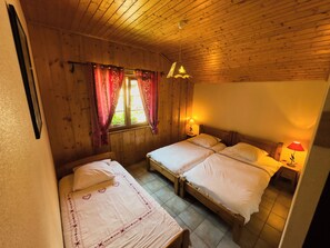 A wooden cabin bedroom with two beds, a window with curtains, and a hanging light fixture. - Gîte l'Essentiel, farmhouse group accommodation with spa and sauna, playground (Arc-sous-Cicon)