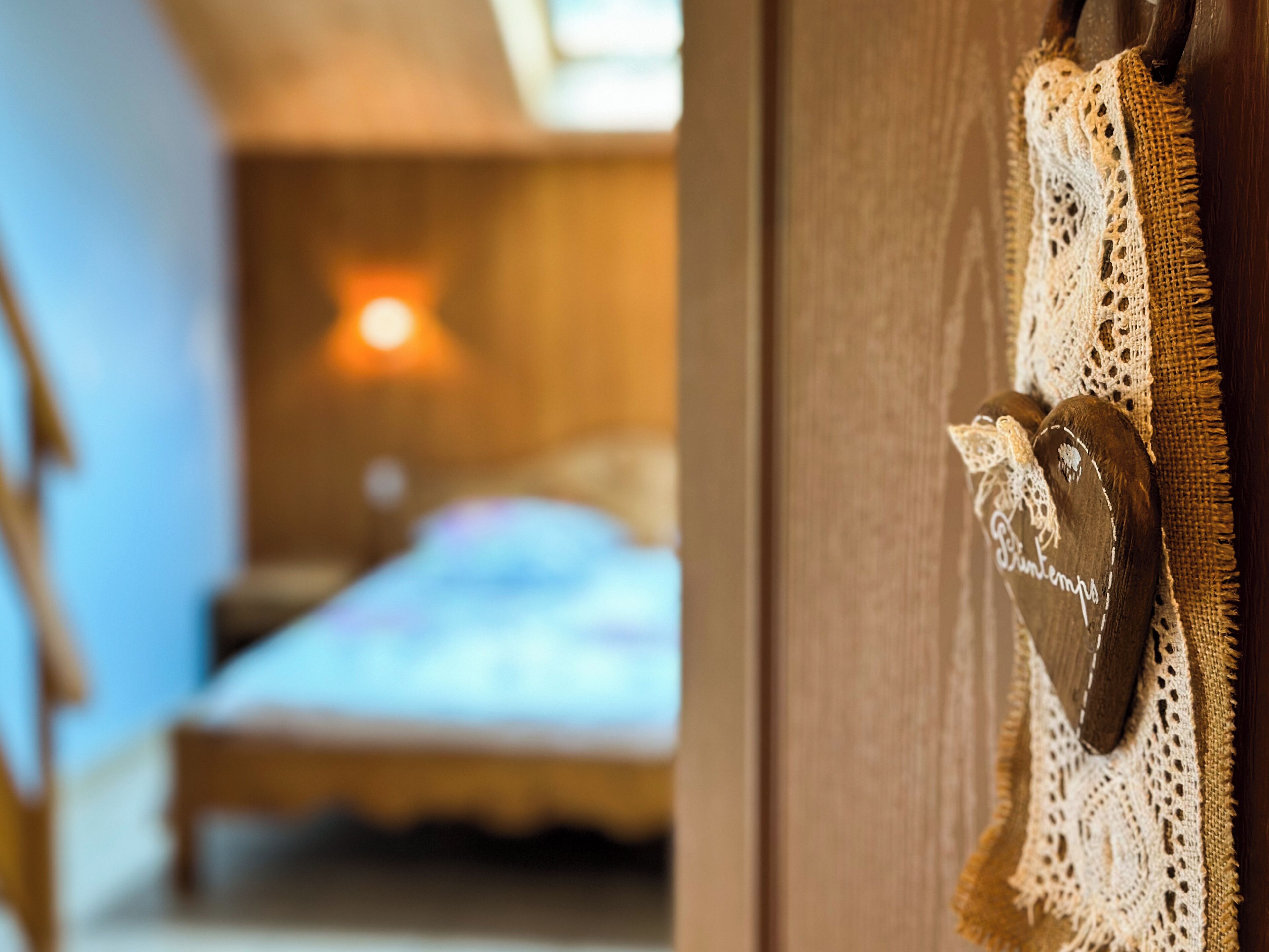 A wooden door with a latch and a doorknob, a lace doormat, and a bed with a white bedspread in the background.