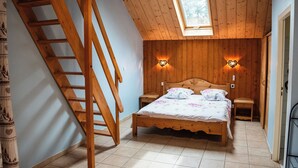 A bedroom with a wooden bed, a skylight, a wooden staircase, and two nightstands with wall-mounted lamps. - Gîte l'Essentiel, farmhouse group accommodation with spa and sauna, playground (Arc-sous-Cicon)