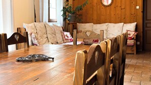 A cozy dining area with a wooden table, chairs, and a sofa with patterned cushions. - Gîte l'Essentiel, farmhouse group accommodation with spa and sauna, playground (Arc-sous-Cicon)