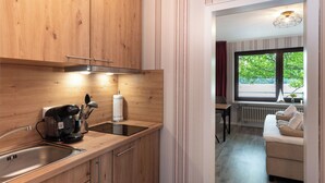 A modern kitchen with wooden cabinets, a built-in stove, and a window overlooking a green area. - Quartier 9 apartment in a quiet location and access to the sea time (Büsum)