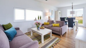 Una sala de estar moderna con un sofá, sillones, una mesa de centro y un comedor con una mesa y sillas.