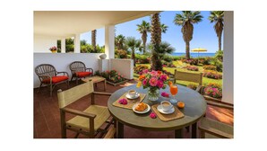 A terrace with a table set for breakfast, overlooking a garden with palm trees and flowers, and a view of the sea. - Awesome apartment in Briatico with house sea view (Briatico)