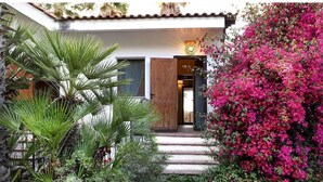 A house with a wooden door, a staircase leading to the entrance, and a garden with green plants and pink flowers. - Awesome apartment in Briatico with house sea view (Briatico)