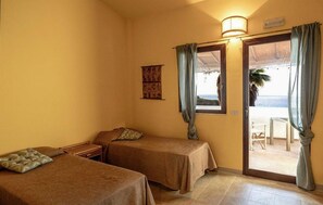 Una habitación con dos camas, una mesita, una ventana con cortinas y vistas a la playa.