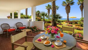 Une terrasse avec une table dressée pour le petit-déjeuner, donnant sur un jardin agrémenté de palmiers et de fleurs, et offrant une vue sur la mer.