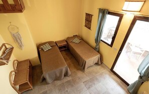 Una habitación pequeña con dos camas individuales, una mesita, una silla y un tapiz de macramé en la pared.