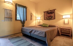 A bedroom with a bed, two bedside lamps, a wall hanging, and a macramé wall hanging.
