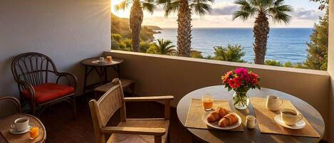A cozy outdoor seating area with wicker chairs and a table set for breakfast, overlooking a scenic ocean view.