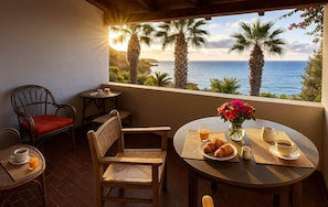 A cozy outdoor seating area with wicker chairs and a table set for breakfast, overlooking a scenic ocean view.