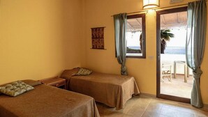 Una habitación con dos camas, una mesita, una ventana con cortinas y vistas a la playa.