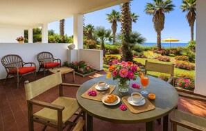 Une terrasse avec une table dressée pour le petit-déjeuner, donnant sur un jardin agrémenté de palmiers et de fleurs, et offrant une vue sur la mer.
