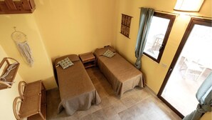 Une petite pièce avec deux lits simples, une petite table, une chaise et une décoration murale en macramé.