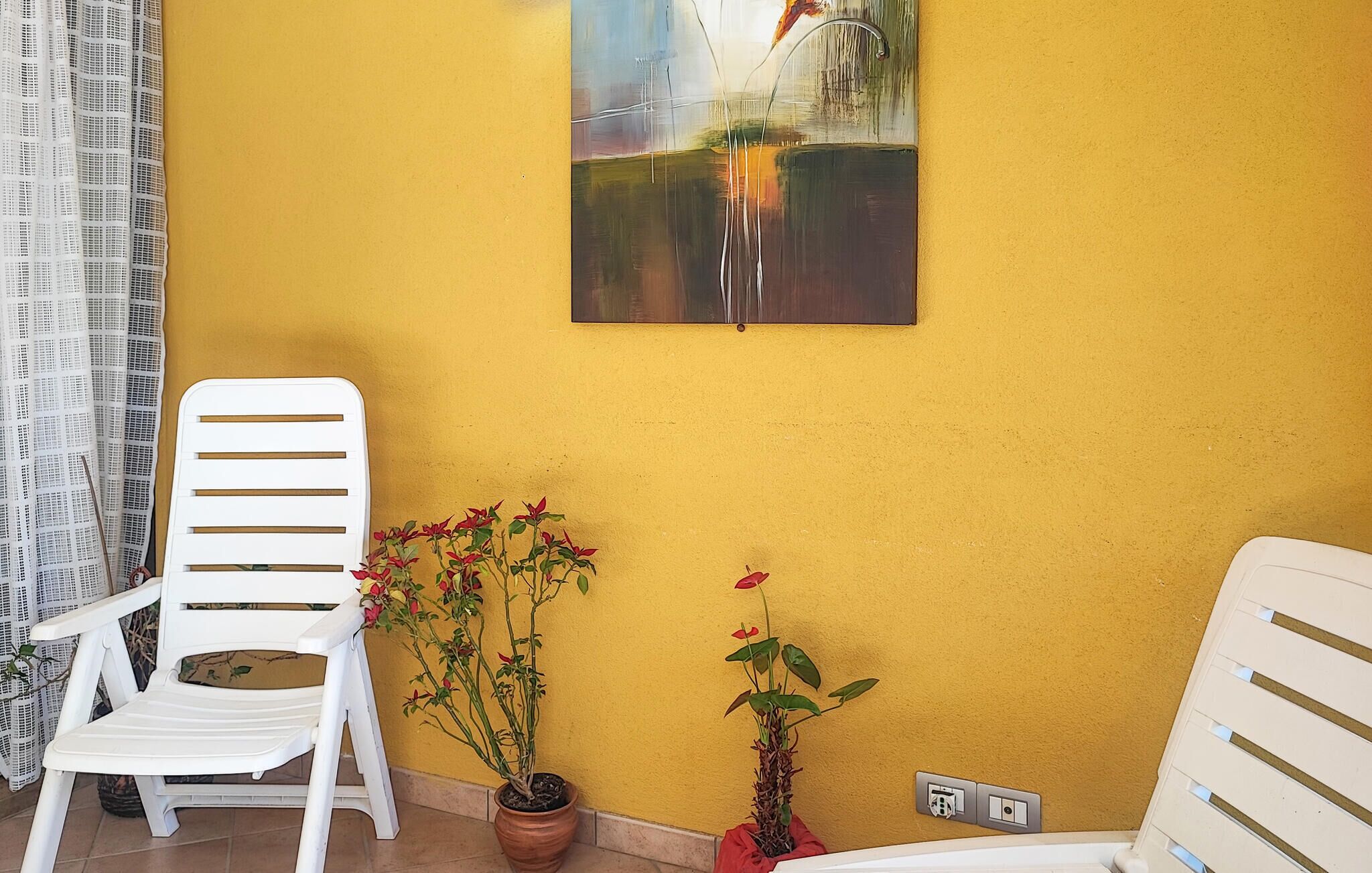 A room with a yellow wall, a white chair, a potted plant, and a painting.