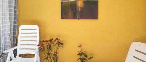 A room with a yellow wall, a white chair, a potted plant, and a painting.
