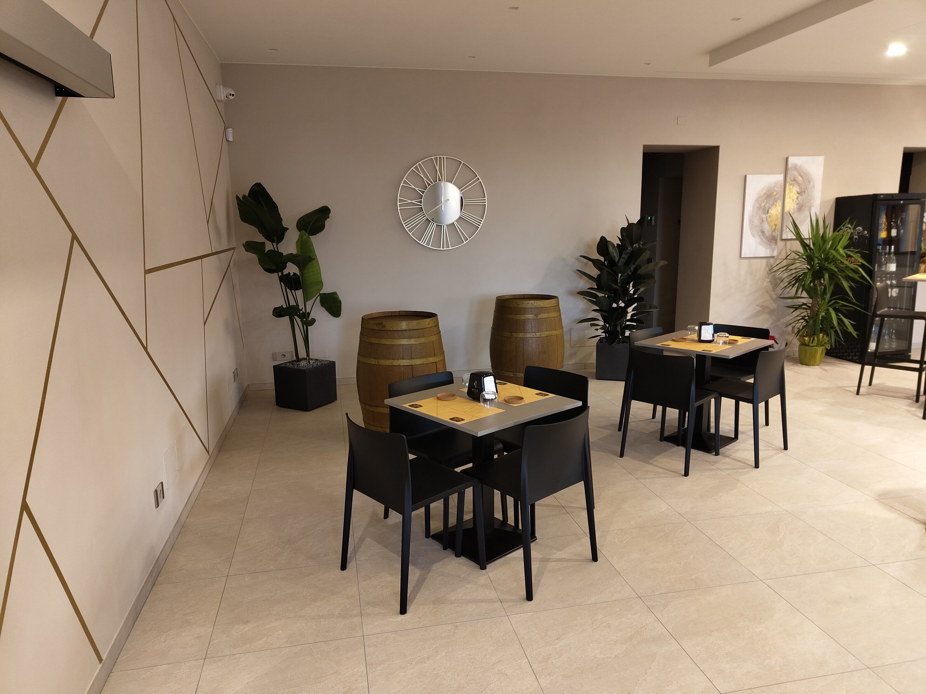 A modern dining area with two tables, black chairs, and decorative elements like a clock and potted plants.