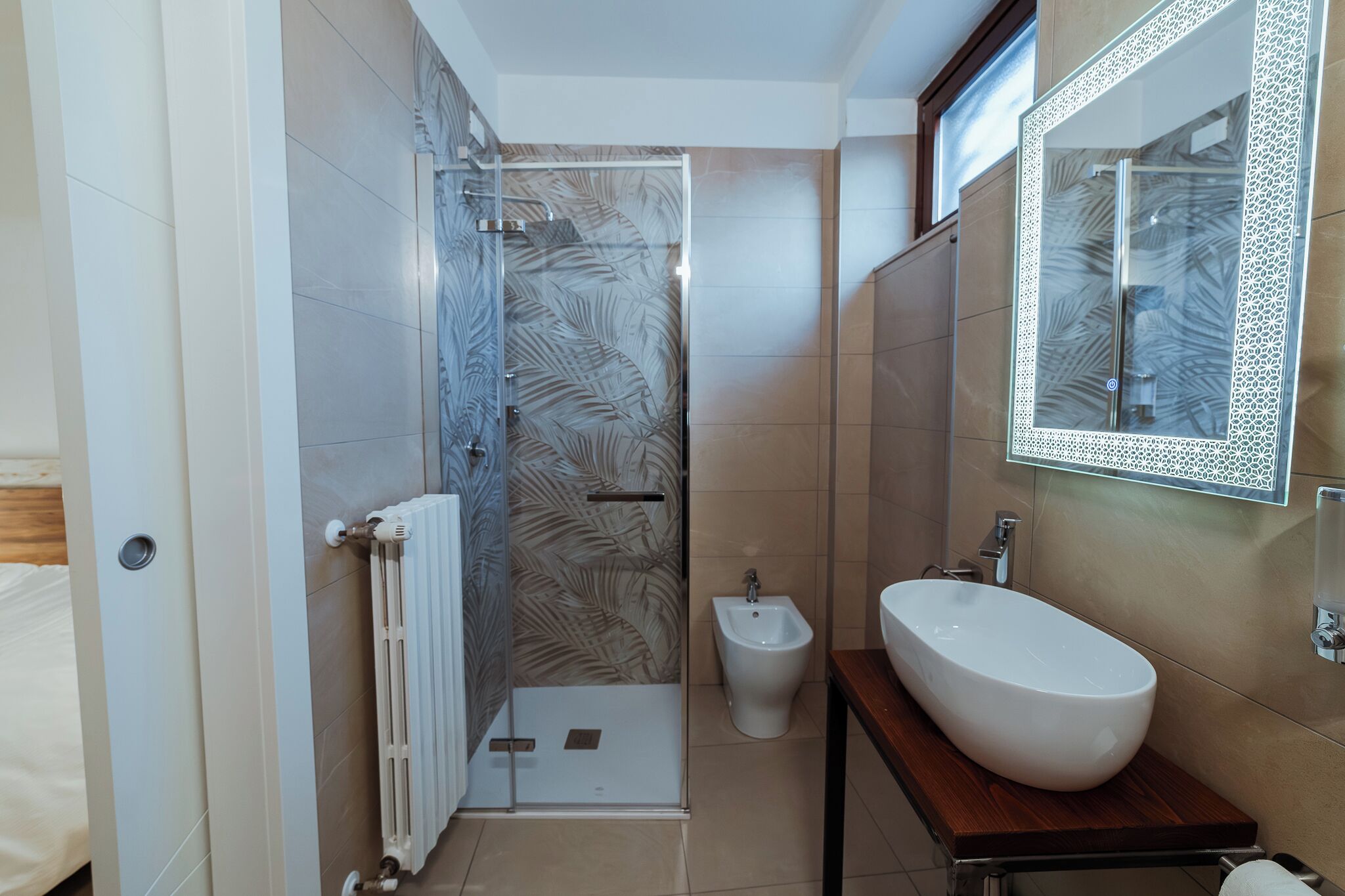 Un bagno moderno con box doccia in vetro, un bidet e un grande specchio con cornice decorativa.