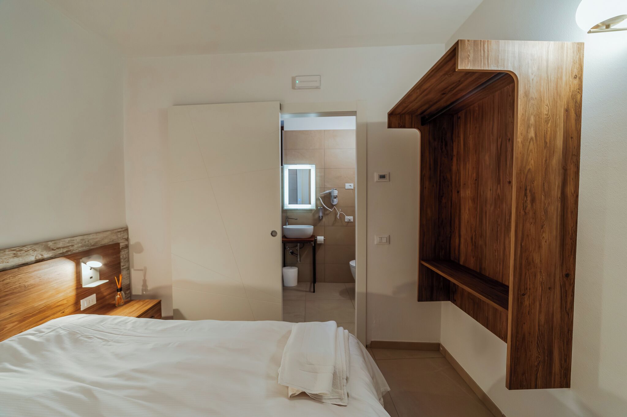 A bedroom with a wooden headboard, a bedside table with a lamp, and a neatly made bed with white linens.