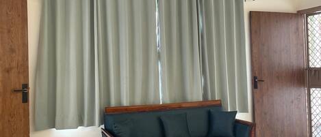 Una habitación con una puerta de madera, un sofá verde, un taburete de madera redondo y un equipo de aire acondicionado blanco en la pared.