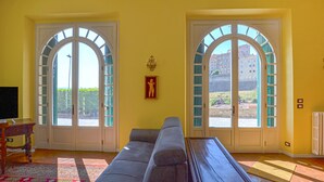 A living room with a sofa, a TV, and two arched windows with shutters.