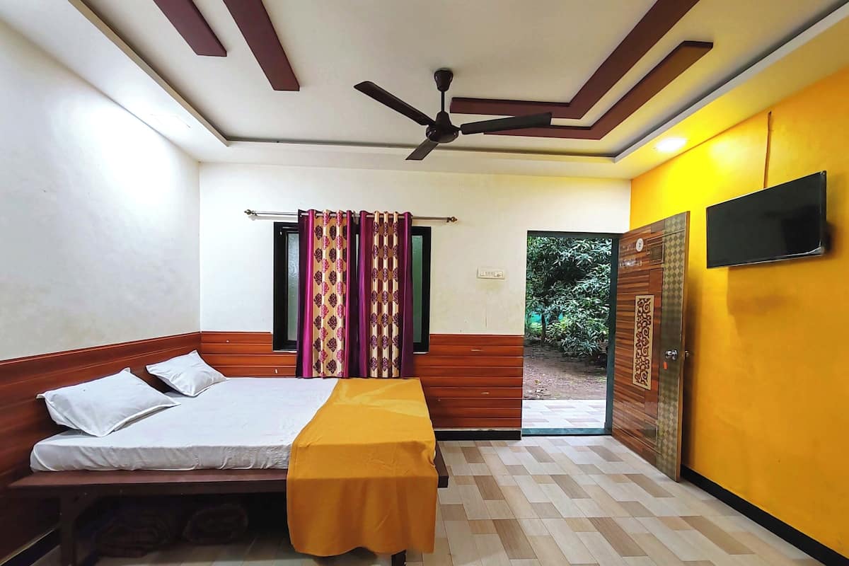 A hotel room with a bed, a bench, a ceiling fan, a TV, and a view of greenery outside.
