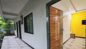 A hallway with a checkered floor, a wooden door with a decorative panel, and a yellow wall. - Lotus Cottage (Alibag)