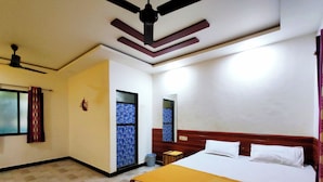 A hotel room with a bed, a ceiling fan, a window with curtains, and a door with a patterned glass panel. - Lotus Cottage (Alibag)