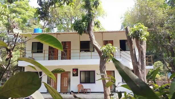A two-story building with a balcony, surrounded by trees. - Lotus Cottage (Alibag)