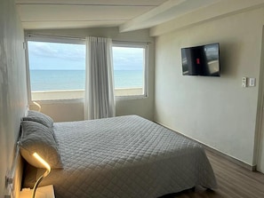 A bedroom with a bed, a TV, and a window with curtains.