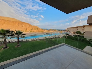A balcony with a view of a swimming pool, palm trees, and a desert landscape.
