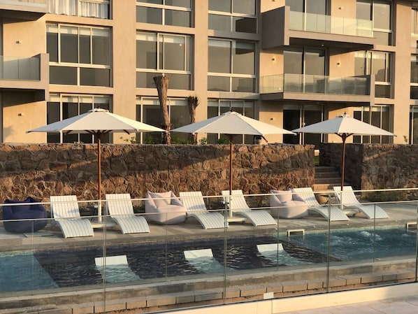A modern hotel with a pool area featuring lounge chairs and umbrellas.