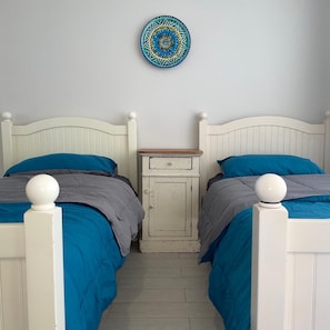 A bedroom with two beds, a nightstand, and a decorative wall hanging.
