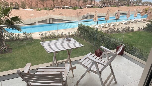 Ein Balkon mit Tisch und zwei Lounge-Stühlen, mit Blick auf einen Pool und eine angelegte Grünfläche.
