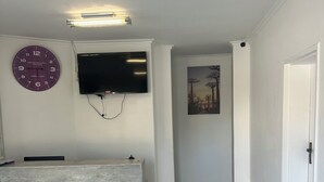 Un área de recepción con suelo de baldosas de mármol, mostrador de recepción, televisor de pantalla plana montado en la pared y un reloj.