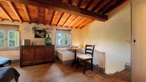 A room with a wooden ceiling, a bench, a chair, a radiator, and a window with a view of greenery.