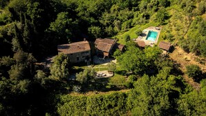 An aerial view of a property with a swimming pool, multiple buildings with tiled roofs, and surrounding greenery.