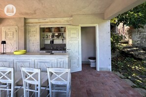 A kitchen with a bar area, white cabinetry, and a stone wall with greenery.