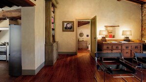 A room with wooden flooring, a desk with a lamp, a chair, and a bookshelf.