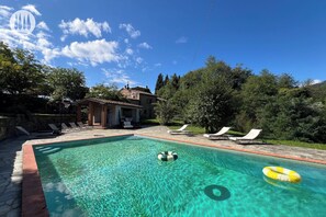 A clear swimming pool with lounge chairs and a small building in the background.
