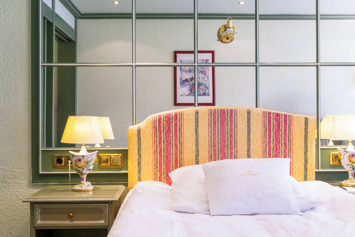A hotel room with a bed, two bedside lamps, a nightstand, and a wall-mounted lamp.