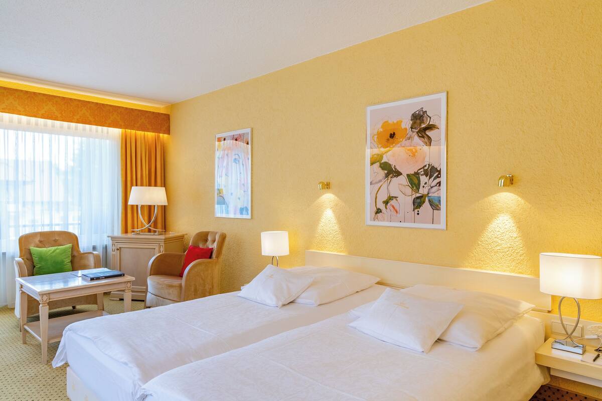 A hotel room with two beds, a desk, a chair, and two lamps.
