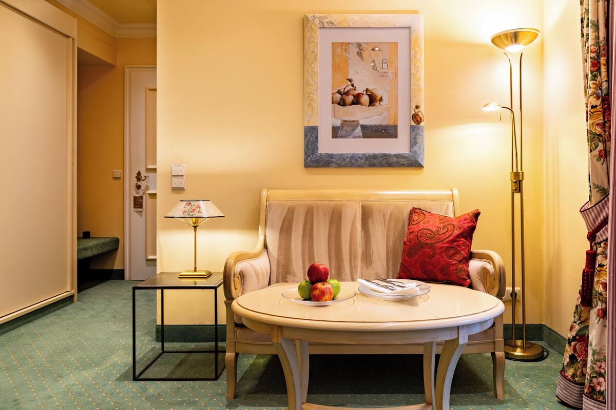 A room with a sofa, a small table with fruit, a framed picture on the wall, and a floor lamp.
