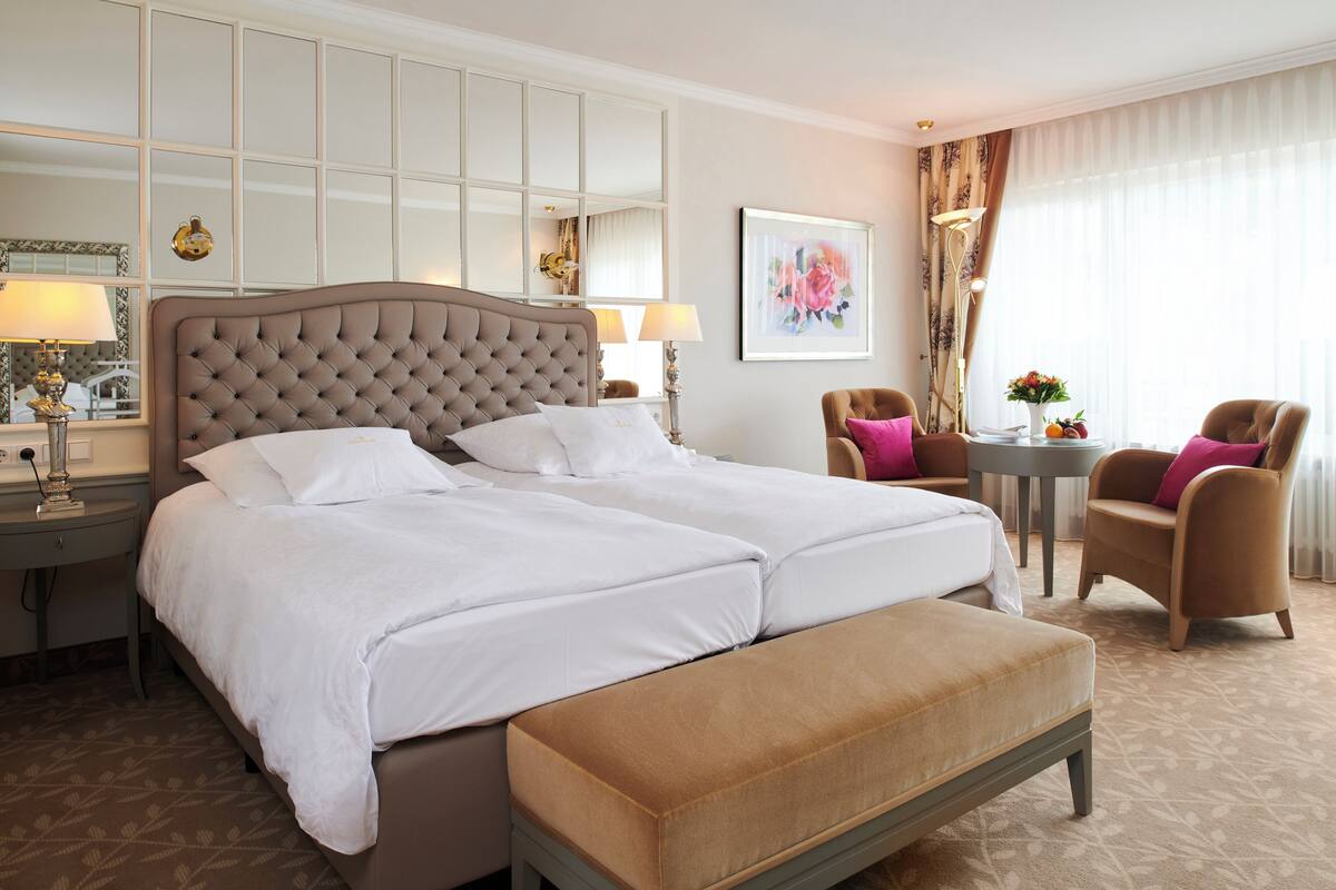 A hotel room with a large bed, a bedside table, a chair, a desk, and a window with curtains.