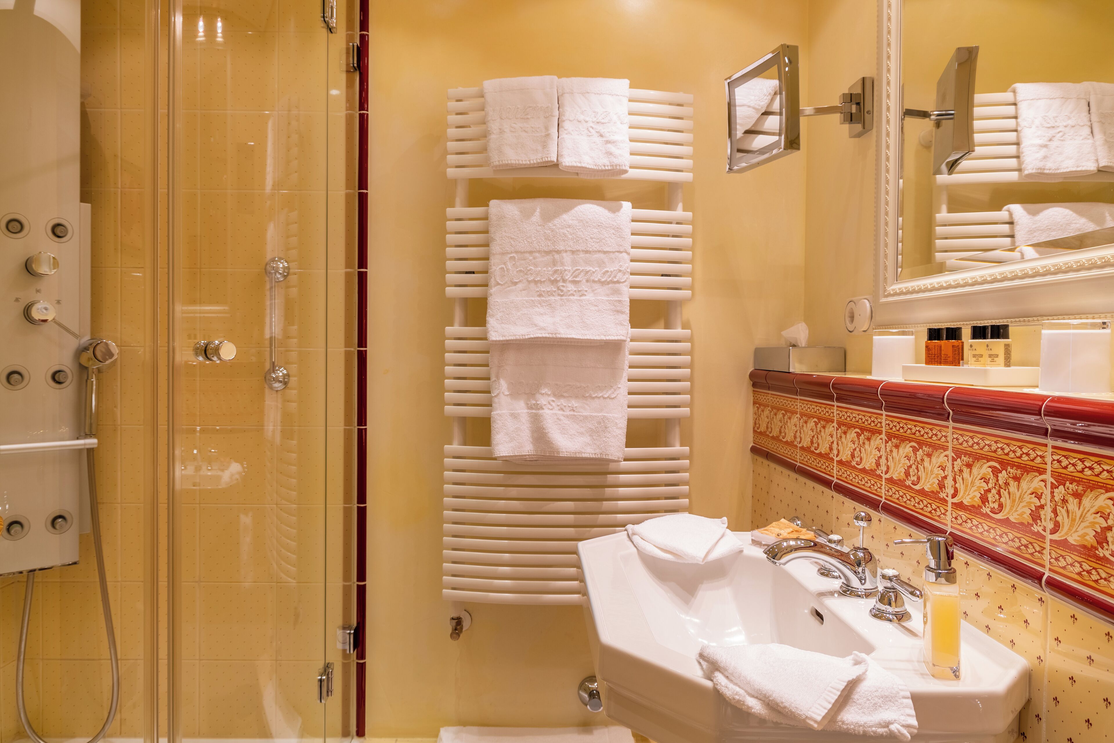 A bathroom with a glass shower enclosure, a white sink with a mirror, and multiple white towels on a rack.