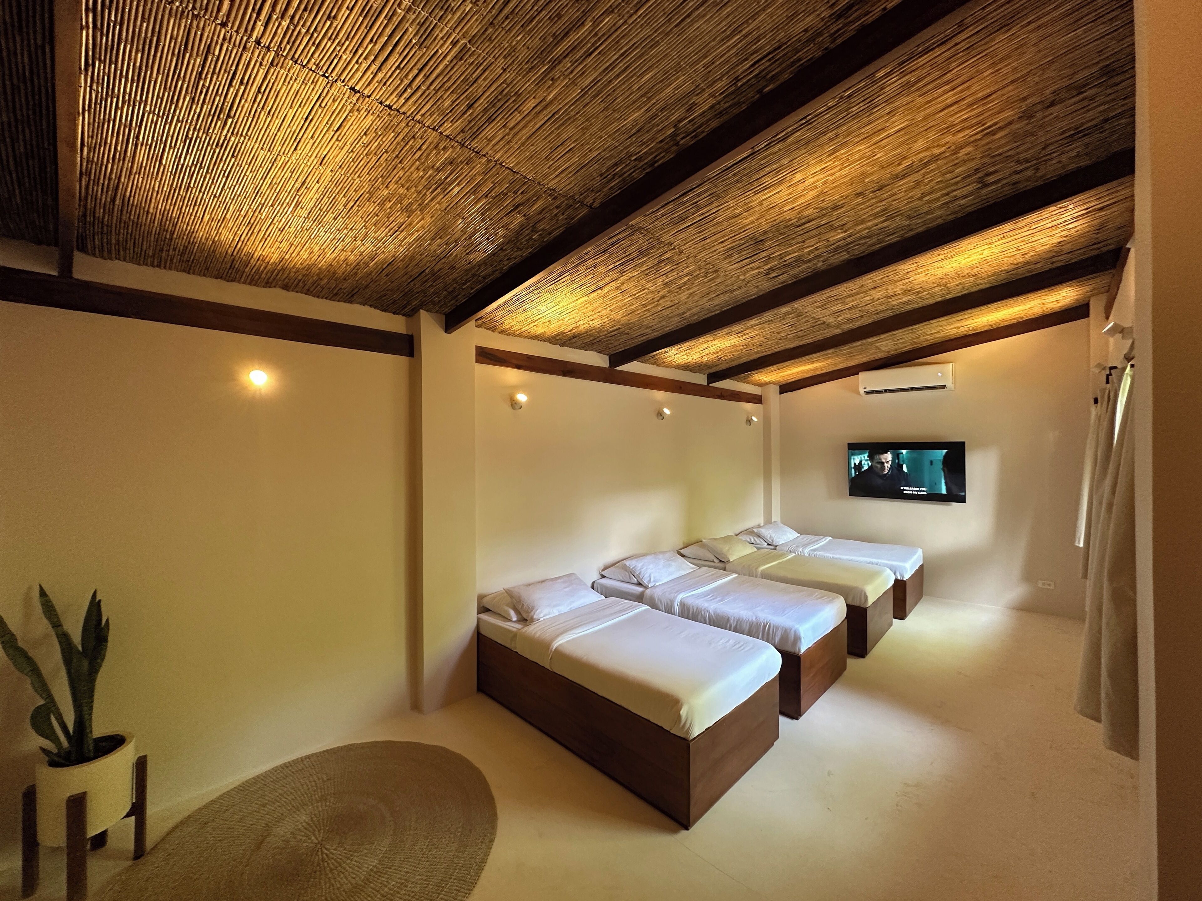 A room with three beds, a television, and a ceiling with a woven design.